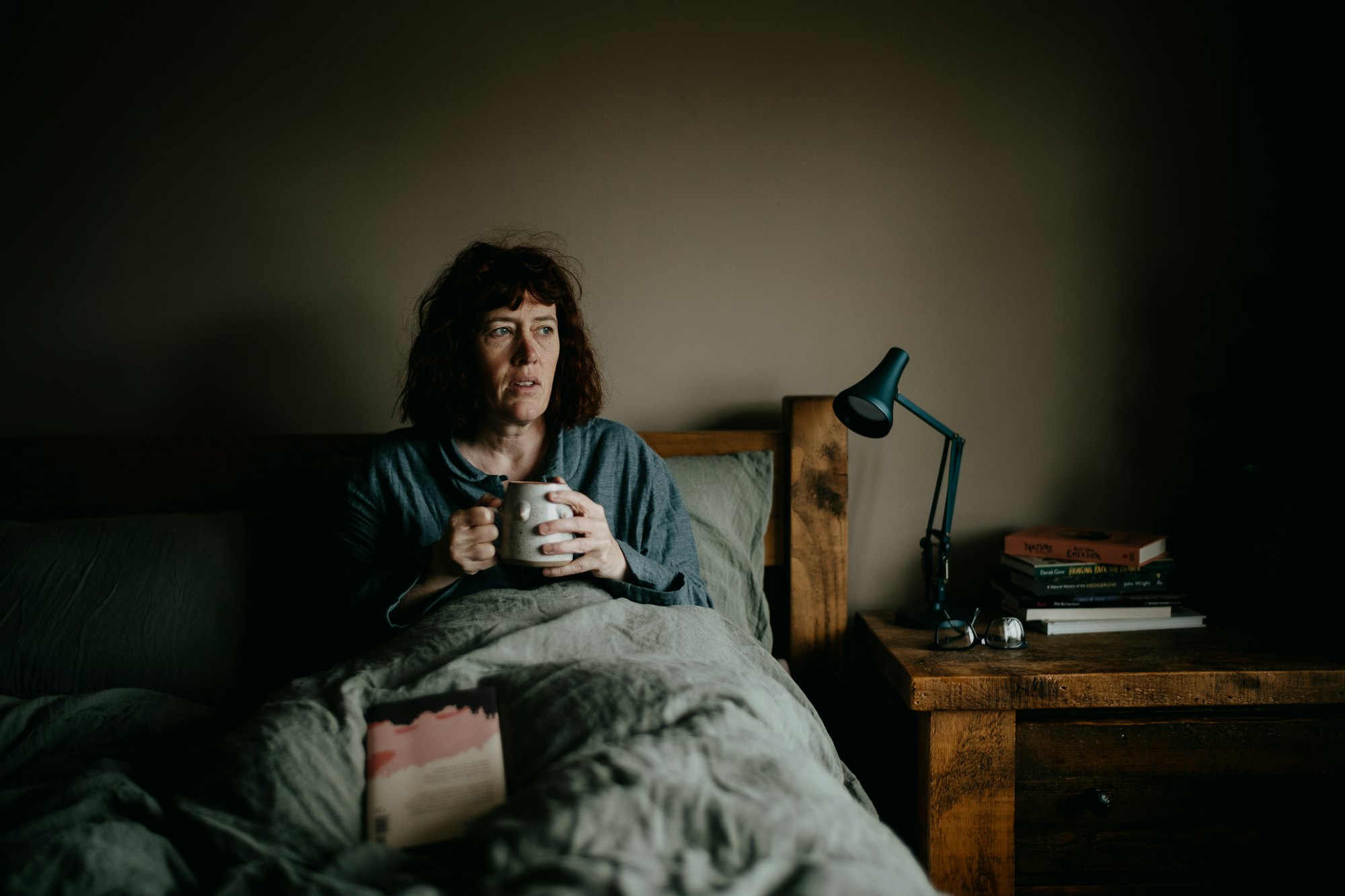 A woman resting in bed with a hot drink